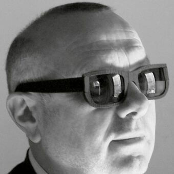 Head-mounted device, black and white, angular glasses with rectangular protrusions worn by Denis Santachiara in portrait.