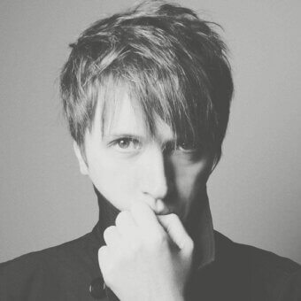 Grayscale portrait of a person with short hair gazing forward, hand lightly touching lips against a plain light background