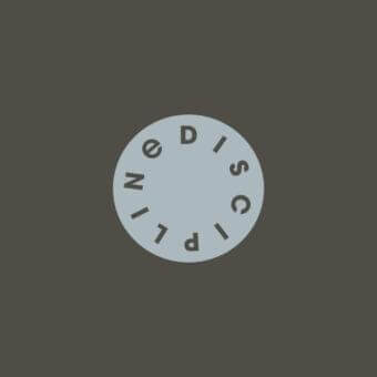 Pale blue-grey circle centered on a grey-brown background contains dark grey sans-serif lettering spelling “DISCIPLINØ” around its edge