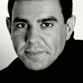 Centered face of a middle-aged man with dark hair and a neutral expression against a light gray backdrop