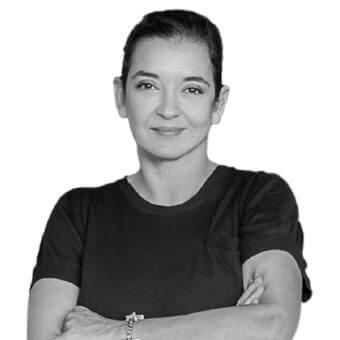 Monochrome portrait of a person with dark hair and light skin, arms crossed, wearing a dark garment against a light gray backdrop
