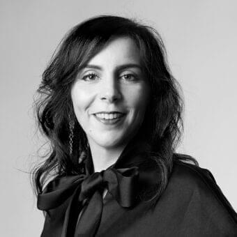 Grayscale portrait of a woman with dark wavy hair and a slight smile wearing a dark garment with a tied bow