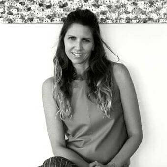 Grayscale portrait of a smiling woman in patterned clothing leaning against a textured surface with a repeating dark geometric design