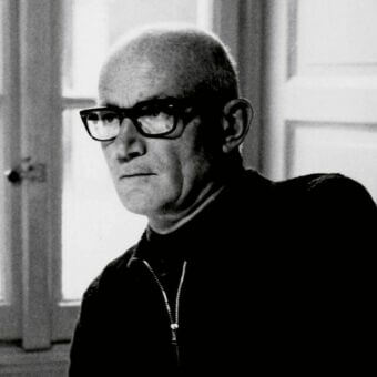 Black and white portrait of Guido Faleschini wearing a dark turtleneck, with a white door and brass knob in the background.