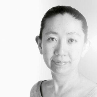 Black and white portrait of Kazuyo Komoda, knit top, smooth complexion, expressive eyes, gentle smile, minimalist white background, soft lighting.