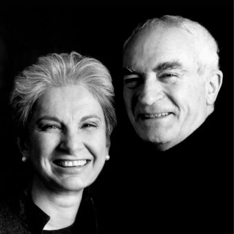 Two smiling faces are centered against a dark background with focused lighting and visible facial details