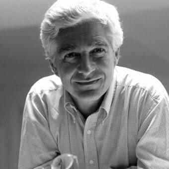 Grayscale portrait of a man with short hair wearing a checkered shirt and glasses on a nearby surface