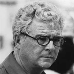 Gray scale portrait of a mature man with wavy hair wearing oval glasses and a dark textured garment