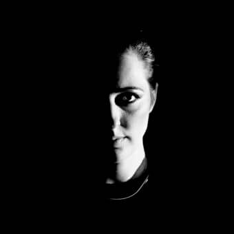 Black and white portrait of Margherita Fanti, chiaroscuro lighting, dark turtleneck, direct gaze, minimalist composition, dramatic shadows.