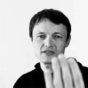 Fair-skinned face with dark short hair looks upward, partially obscured by a blurred pale elongated shape against a white background