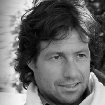 Massimo Tonetto portrait, black and white, wavy dark hair, turtleneck sweater, light scarf, blurred garden background, soft lighting.