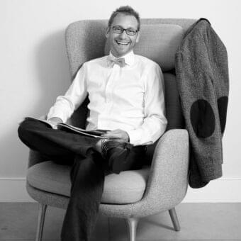 Seated person facing forward wearing a patterned bow tie and light shirt in a grayscale image