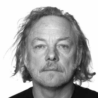 Grayscale portrait of a middle-aged man with wavy hair, mustache, and visible facial lines against a plain white backdrop