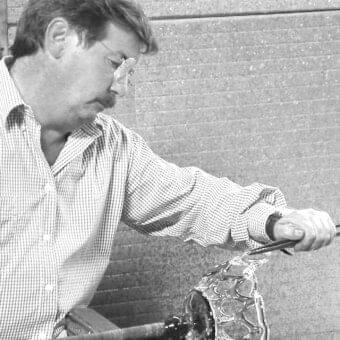 Man with glasses holds a textured, translucent object with raised lines over a mottled gray surface
