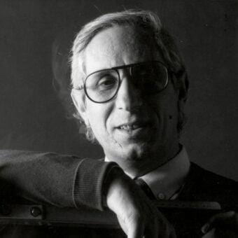 Pierluigi Molinari portrait, man in suit and glasses holding a black camera, dark gradient background, soft diffused lighting.