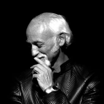 Ross Lovegrove portrait, black and white photograph, man with beard wearing textured leather jacket, contemplative expression, profile view.