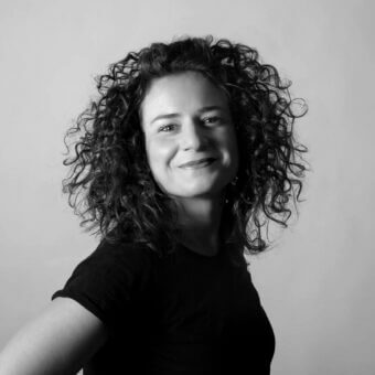 Black and white portrait of Silvia Musetti with curly dark hair, wearing a black t-shirt and necklace against a light gray gradient backdrop.