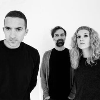 Monochromatic head and shoulders portrait of three people facing forward against a light gray backdrop