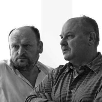 Two men with receding hairlines are shown from the chest up against a light, vertically lined background in grayscale