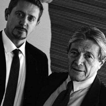 Grayscale portrait of two formally dressed men with a striped graphic backdrop and diffused lighting