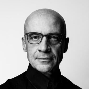 Claudio Bellini portrait, black and white, bald man with glasses, black collared shirt, formal headshot, neutral expression, white background.