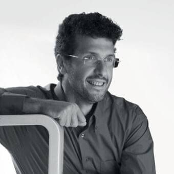 Grayscale portrait of a man with curly hair wearing glasses and a collared shirt looking slightly upward and to the side