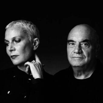 Grayscale close-up of two heads with differing hairlines facing each other against a dark, blurred backdrop