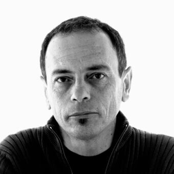 Francesco Bettoni portrait, black and white, dark ribbed knit sweater, direct gaze, stark white background, even lighting, detailed facial features.