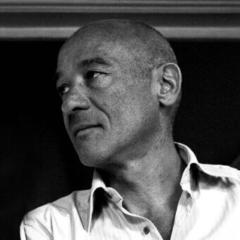 Black and white portrait of Francesco Rota, bald man with freckles, wearing a light shirt, directional lighting, dark indistinct background.
