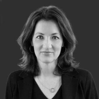 Shoulder-length wavy hair and silver jewelry on a woman with a neutral expression against a dark gray background in grayscale