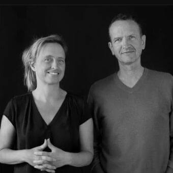 Close-up grayscale portrait of two people facing forward with gentle smiles against a dark background
