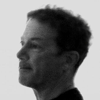 Black and white portrait of Guido Rosati in profile, light gray background, grainy texture, short tousled hair, contemplative expression.