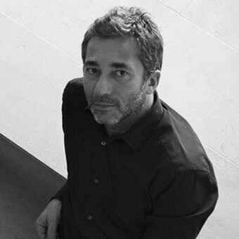 Black and white portrait of Leonardo Dainelli, a man with short dark hair and a salt-and-pepper beard, wearing a dark button-down shirt.