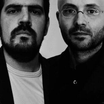 Grayscale portrait of two men facing each other with beards and glasses against a light neutral background