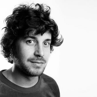 Portrait of Lorenzo De Bartolomeis, a man with dark curly hair and beard, wearing a black t-shirt against a plain white background.