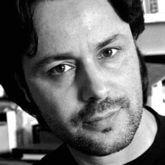 Monochrome portrait of a man with receding hairline, beard, and mustache looking directly at the camera with soft lighting
