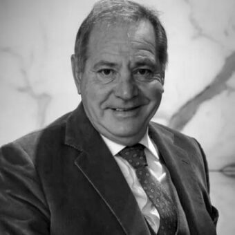 Luciano Lucatello portrait, man in dark suit jacket, white shirt, patterned tie, gray hair, soft lighting, blurred neutral background.