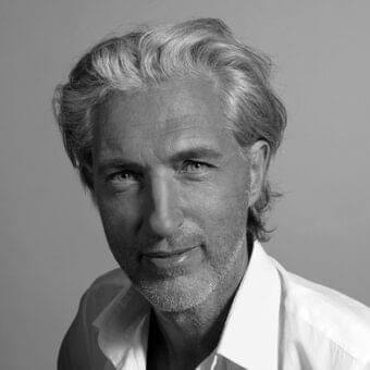 Monochromatic portrait of a man with wavy graying hair and stubble looking forward with a relaxed expression