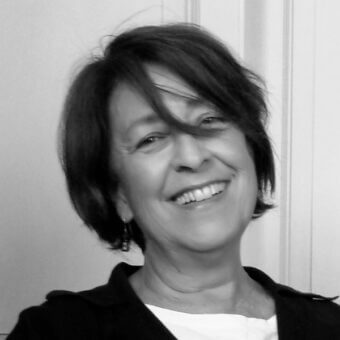 Black and white portrait of a woman with short dark hair, wearing a black jacket and earrings, smiling with soft diffused lighting.