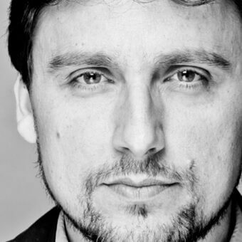 Black and white portrait of Matteo Ragni with short beard, light gray eyes, neutral expression, against a light gray backdrop.