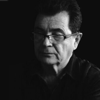 Black and white portrait of Maurice Barilone, a middle-aged man with glasses, wearing a textured dark shirt, studio lighting.