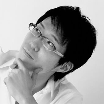 Black and white portrait of a man with glasses, wearing a white shirt, in a light gray studio, gazing off-camera with a contemplative pose.