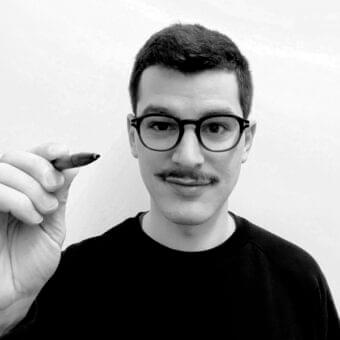Grayscale portrait of a person with short dark hair, round glasses, and a mustache holding a dark cylindrical object upwards