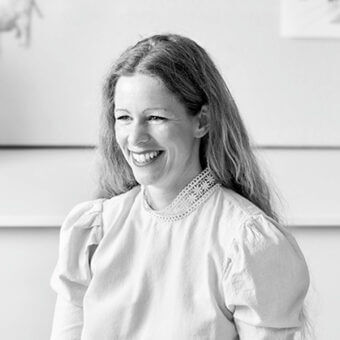 Woman portrait, light blouse with lace collar, soft linen texture, neutral background, diffused lighting, architectural details visible.