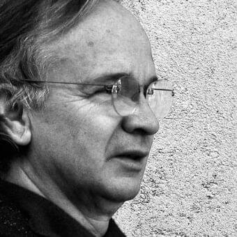 Monochrome portrait of a man in profile with short hair, glasses, and visible facial lines against a textured light background