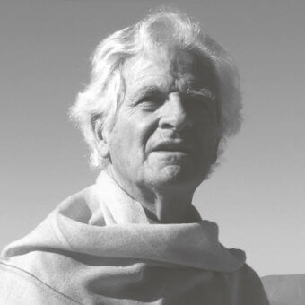 Black and white portrait of an elderly man with wavy white hair, wearing a light shawl, against a light gray background with “pierre paulin” text.
