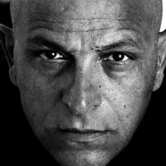 Close-up black and white portrait of a middle-aged man with shaved head and direct gaze showing facial lines and skin texture