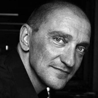 Close-up black and white portrait of a mature man facing forward with short hair and a subtle expression wearing a dark jacket
