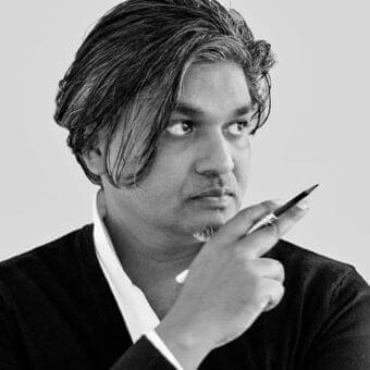 Grayscale portrait of a man with graying dark hair looking right, holding a dark object near his chin against a light background