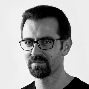 Black and white portrait of Victor Vasilev, wearing rectangular glasses and a gray-flecked beard, against a light gray backdrop.